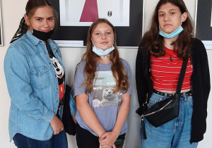 Trzy dziewczyny stoją na tle plakatu poświęconemu twórczości Lema.